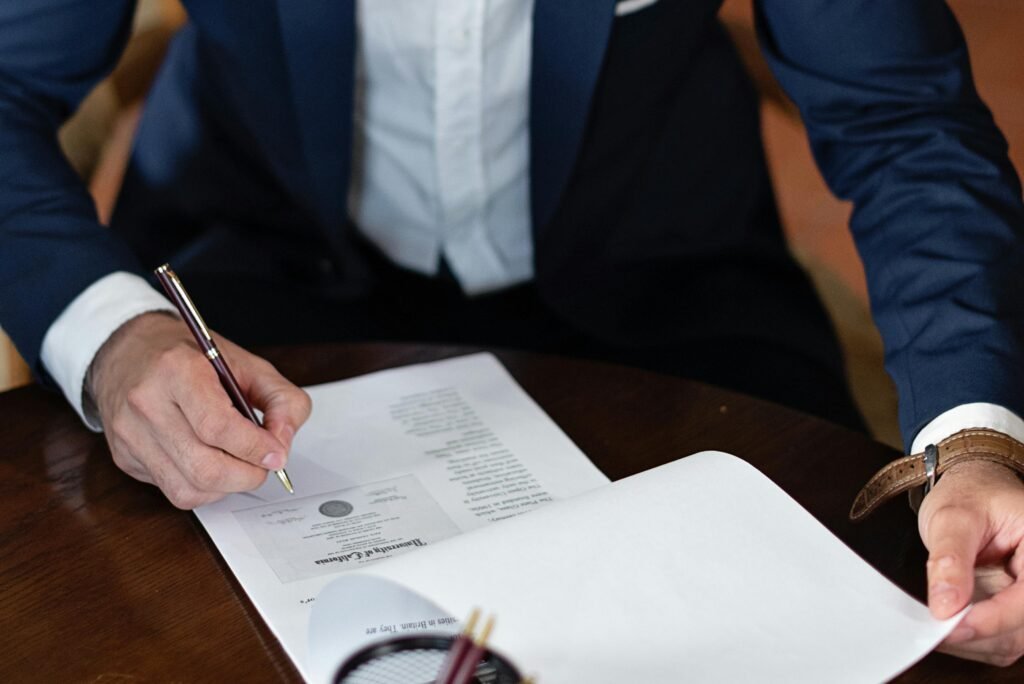 A professional individual signs legal documents at a desk in an office setting.